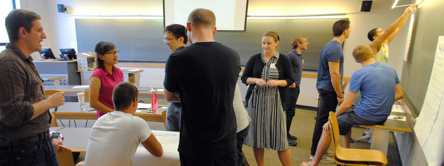 graduate students in a classroom talking to one another and working on the board.